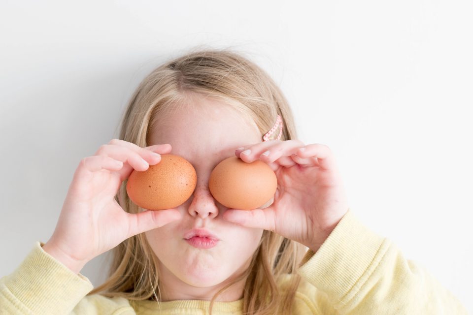 a young child playing with eggs over their eyes