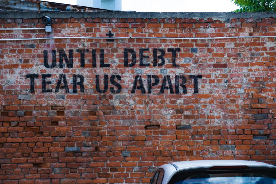 a brick wall with words that read 'until debt tear us apart'