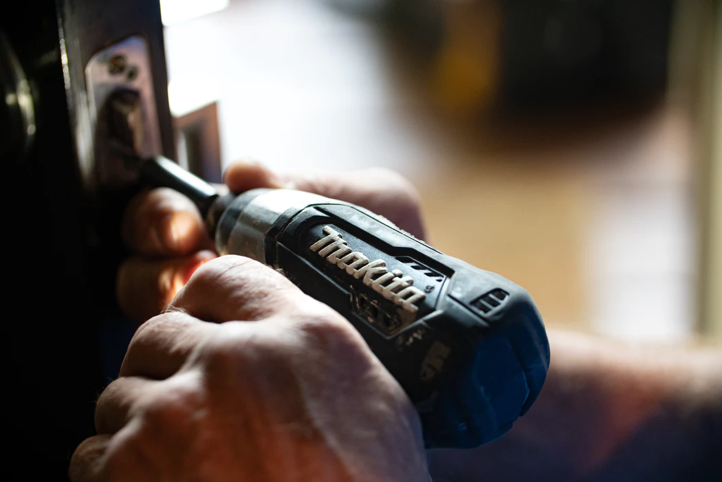 a person fixing a door handle with an electric screwdriver