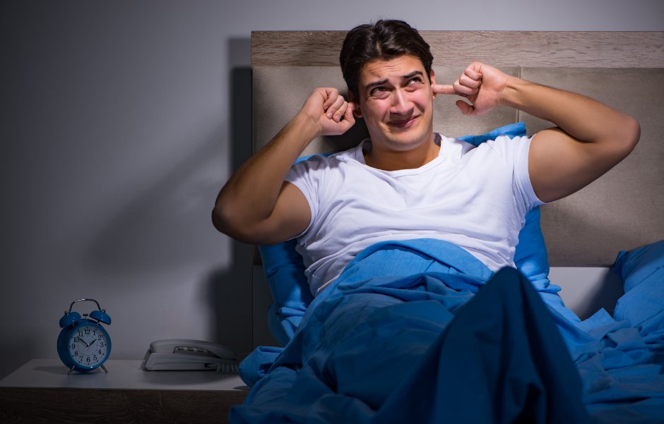 man laying in bed with hands covering ears to block out noise