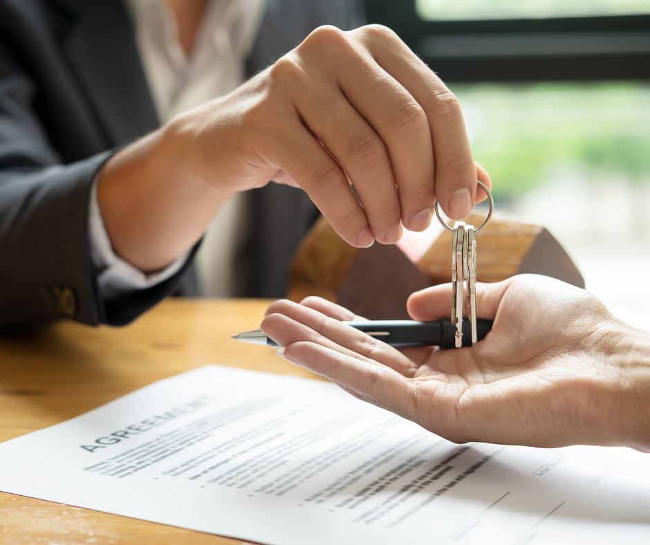 a person in a suit handing over keys after signing a contract