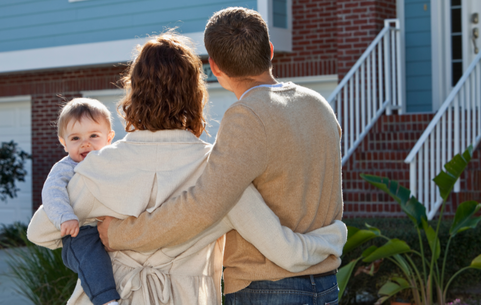 a mum and dad holding a baby standing outside a house