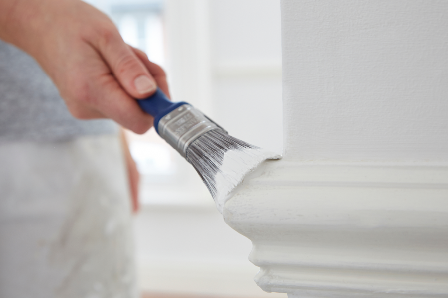 a person touching up a baseboard with paint