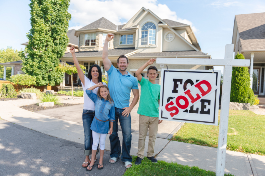 a family cheering in front of a for sale board outside a house