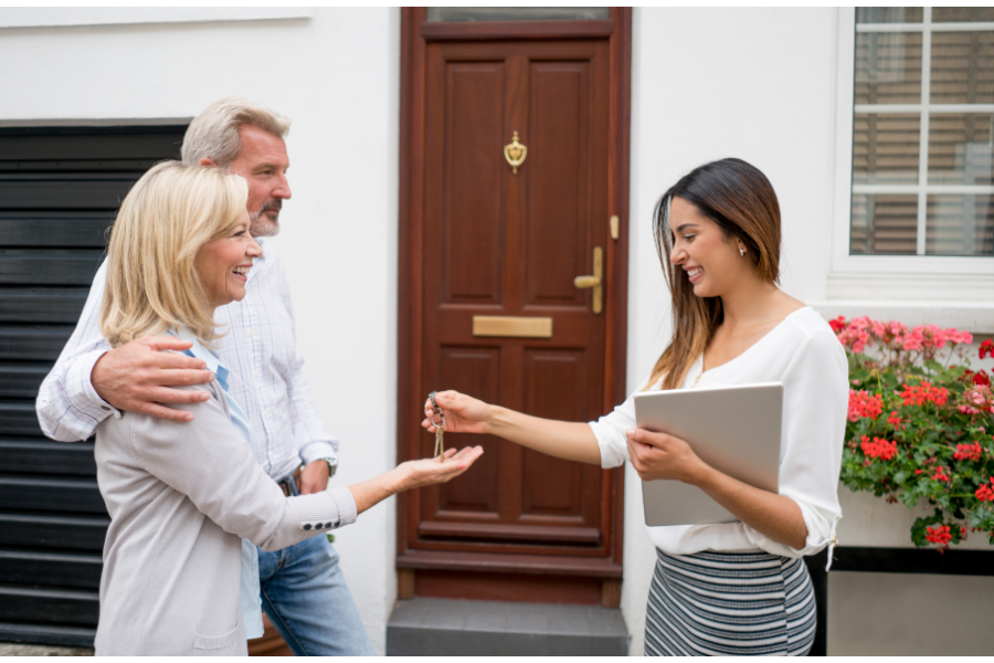 an older couple being handed keys outside a house by a realtor