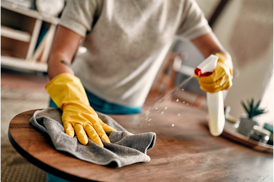 a person spraying cleaner and wiping a wood table