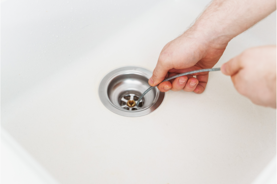 a person using a drain snake on a clogged drain at home