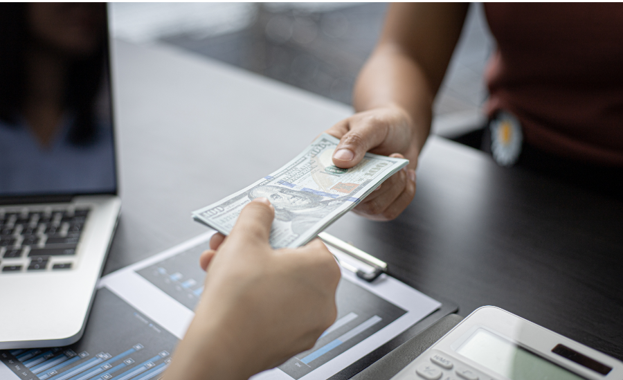 two people exchanging cash in hand over a desk