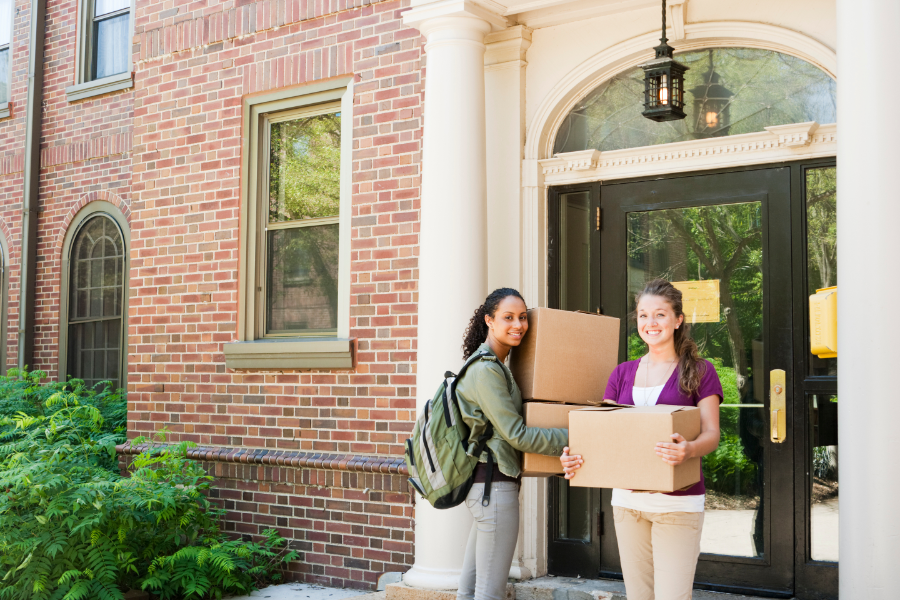 two students holding boxes outside a student house